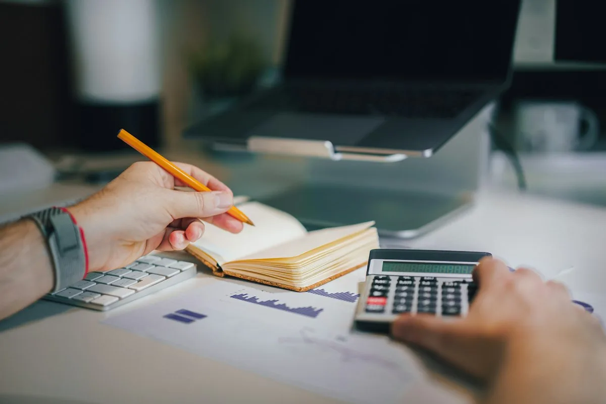 Persona calculando el presupuesto de su negocio con una calculadora y un cuaderno